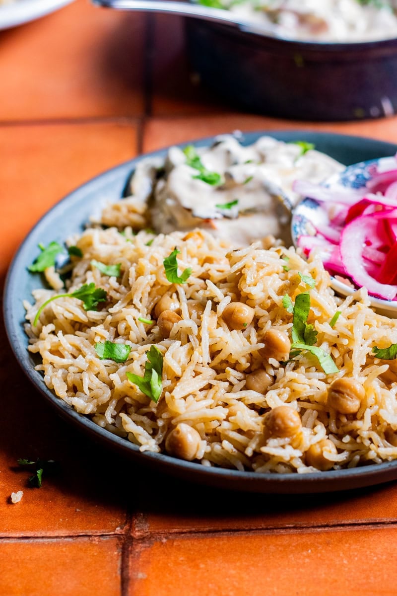 a plate of chana pulao with raita and pickled onions