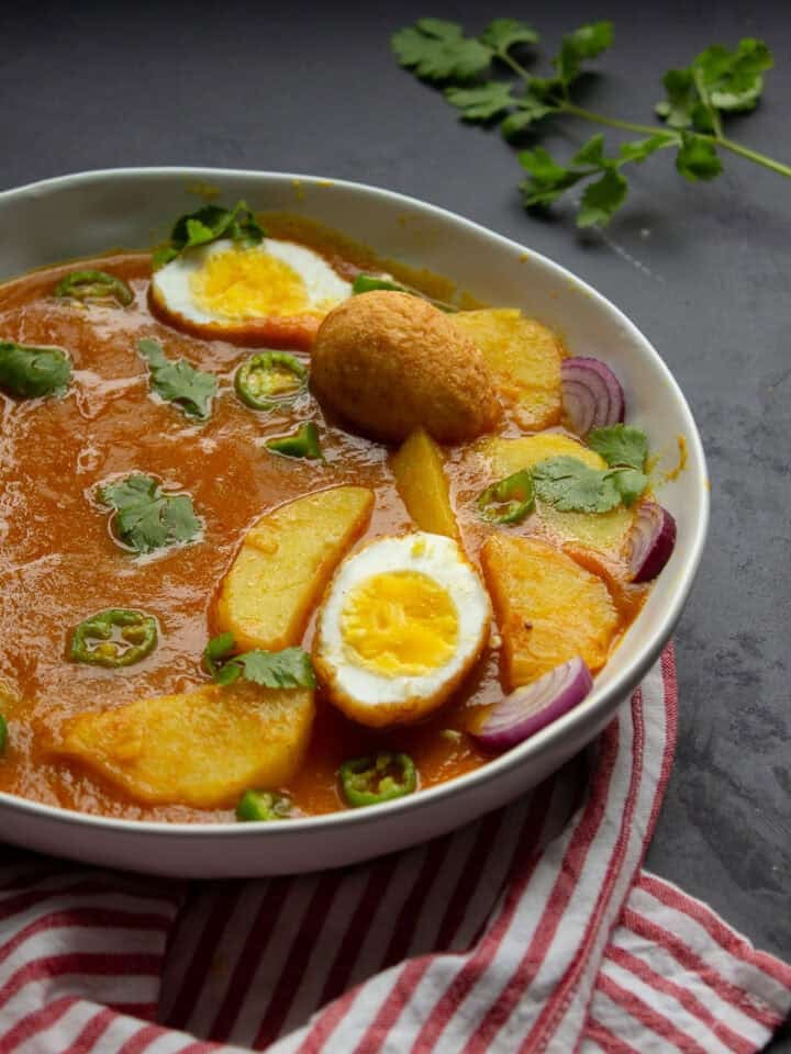a bowl of egg curry or anday aloo ka salan with an egg sliced in half and others left whole