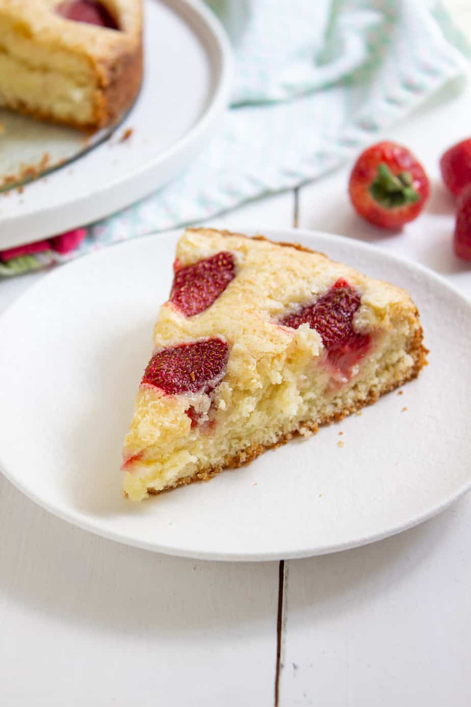 a piece of strawberry cake with a strawberry in the background
