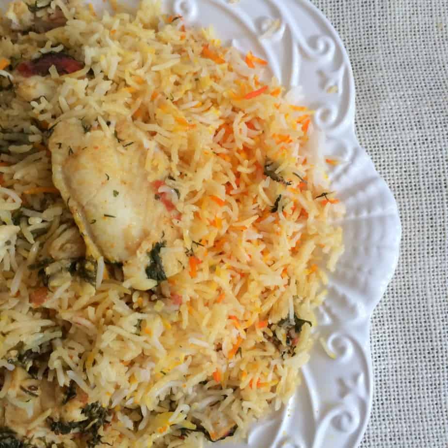 A close-up of a plate of chicken biryani, featuring long-grain rice mixed with chicken pieces, herbs, and spices, served on a white patterned plate on a light textured surface—perfect inspiration for your next biryani recipe.