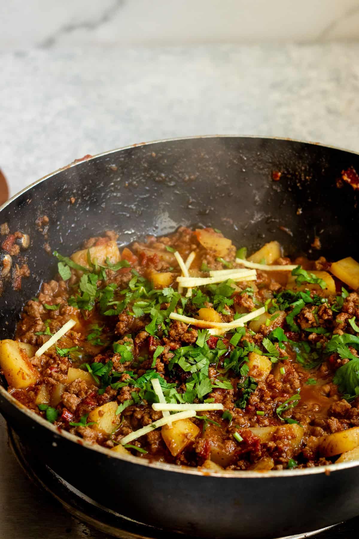 cooked aloo keema in a wok garnished with julienned ginger and cilantro