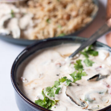 ¾ view of a dish of sabzi raita with a plate of rice in the background