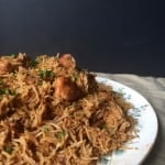 A close-up of a plate filled with kid friendly chicken pulao, garnished with chopped herbs, set against a dark background. The rice appears fluffy and spiced, with visible chunks of chicken.