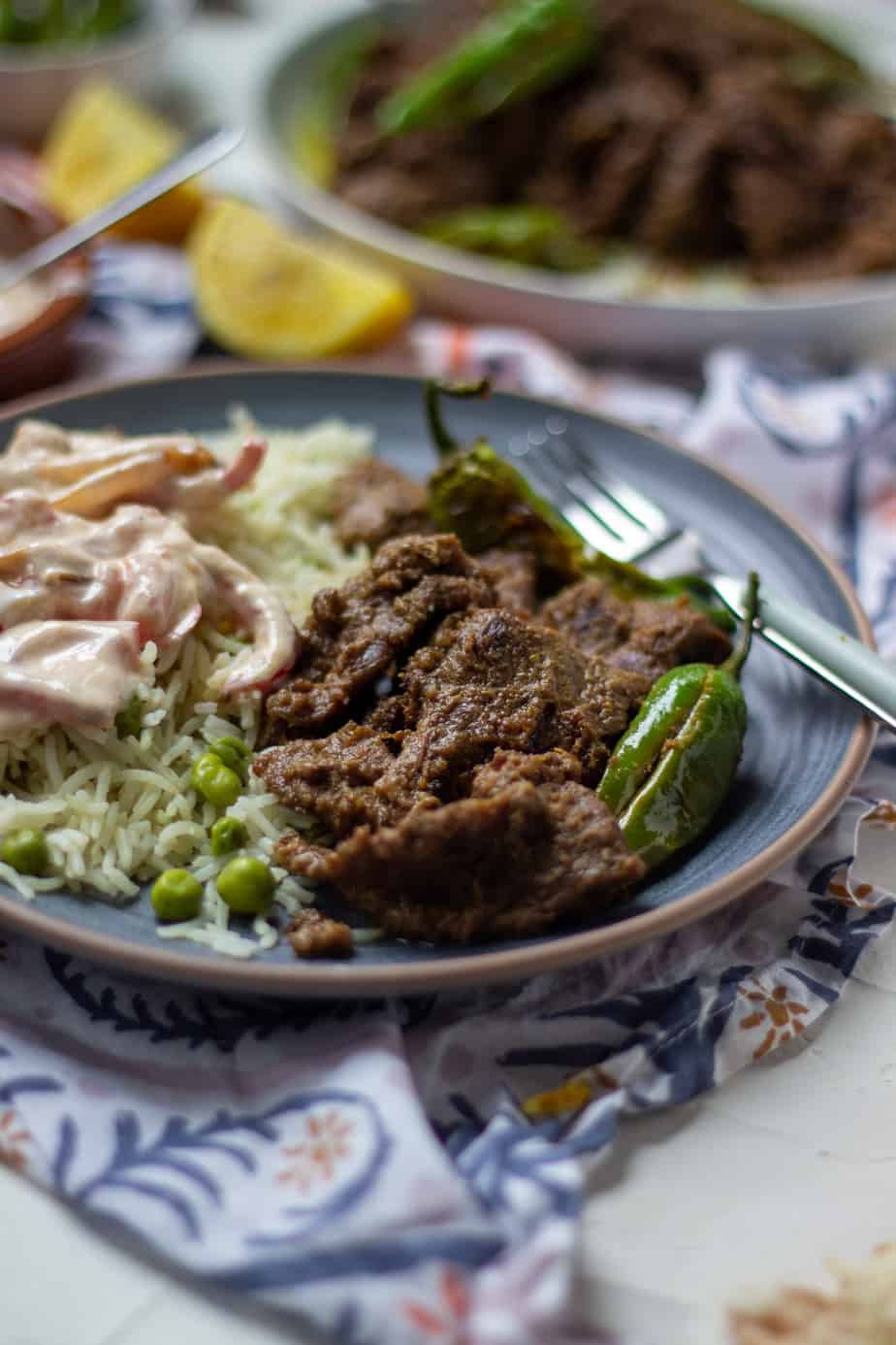 Pasanday on a plate with raita and a patterned napkin underneath