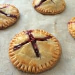 Four golden-brown strawberry Nutella hand pies with crimped edges and X-shaped slits on top, revealing a rich berry filling, rest on a sheet of parchment paper.