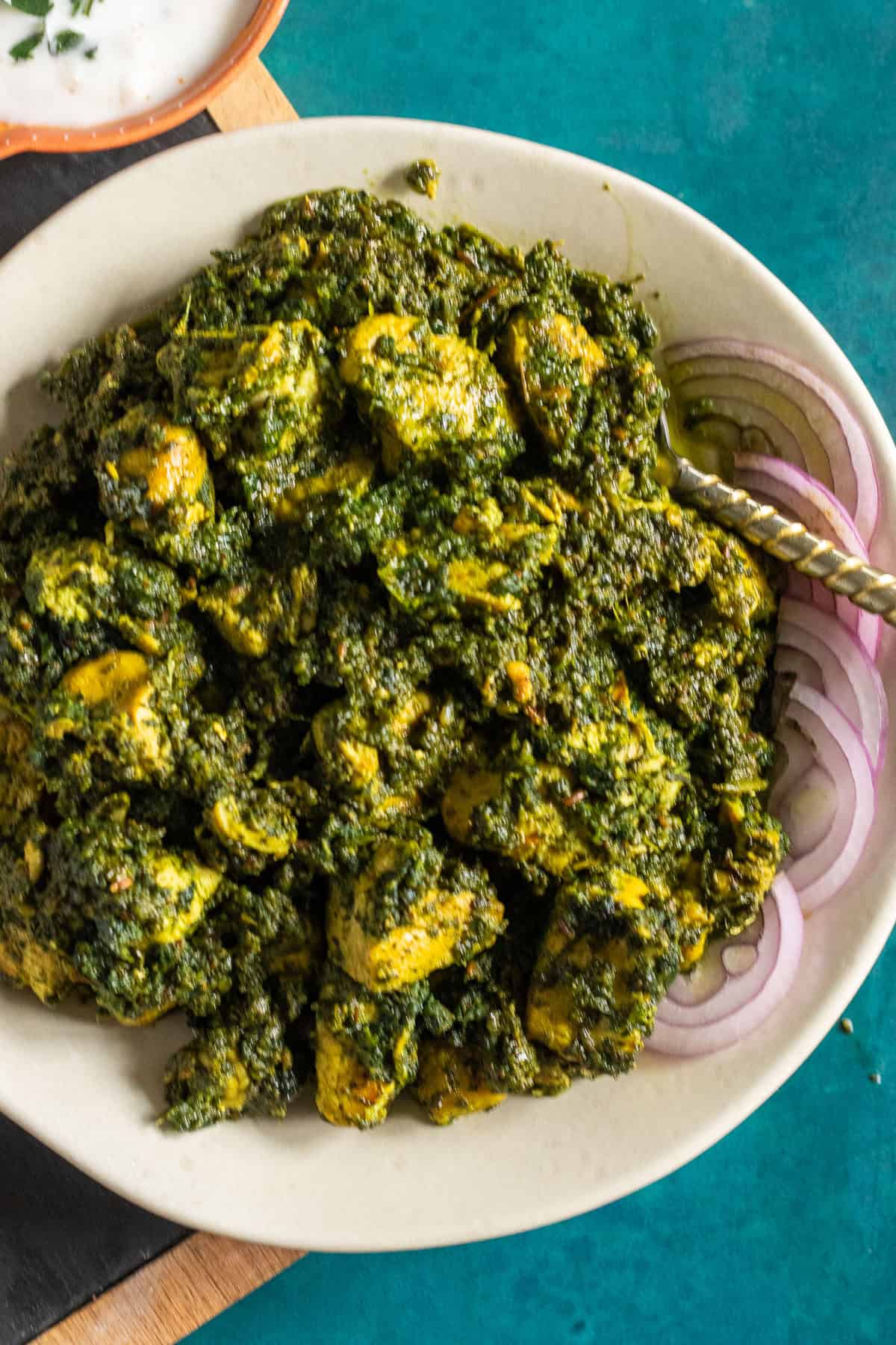 A dish of Palak Chicken garnished with red onions