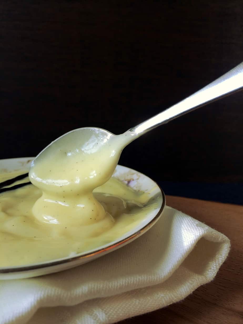 A spoon scooping thick, creamy custard from a shallow dish, with a white napkin underneath the dish and a dark background.