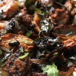 Close-up of caramelized shallots with coconut and tamarind, cooked with spices, curry leaves, and garnished with chopped cilantro, served on a white plate.