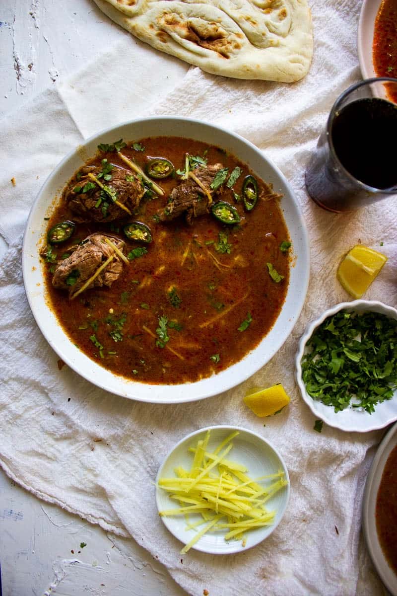 a plate of nihari and little bowls of ginger and cilantro and a coke