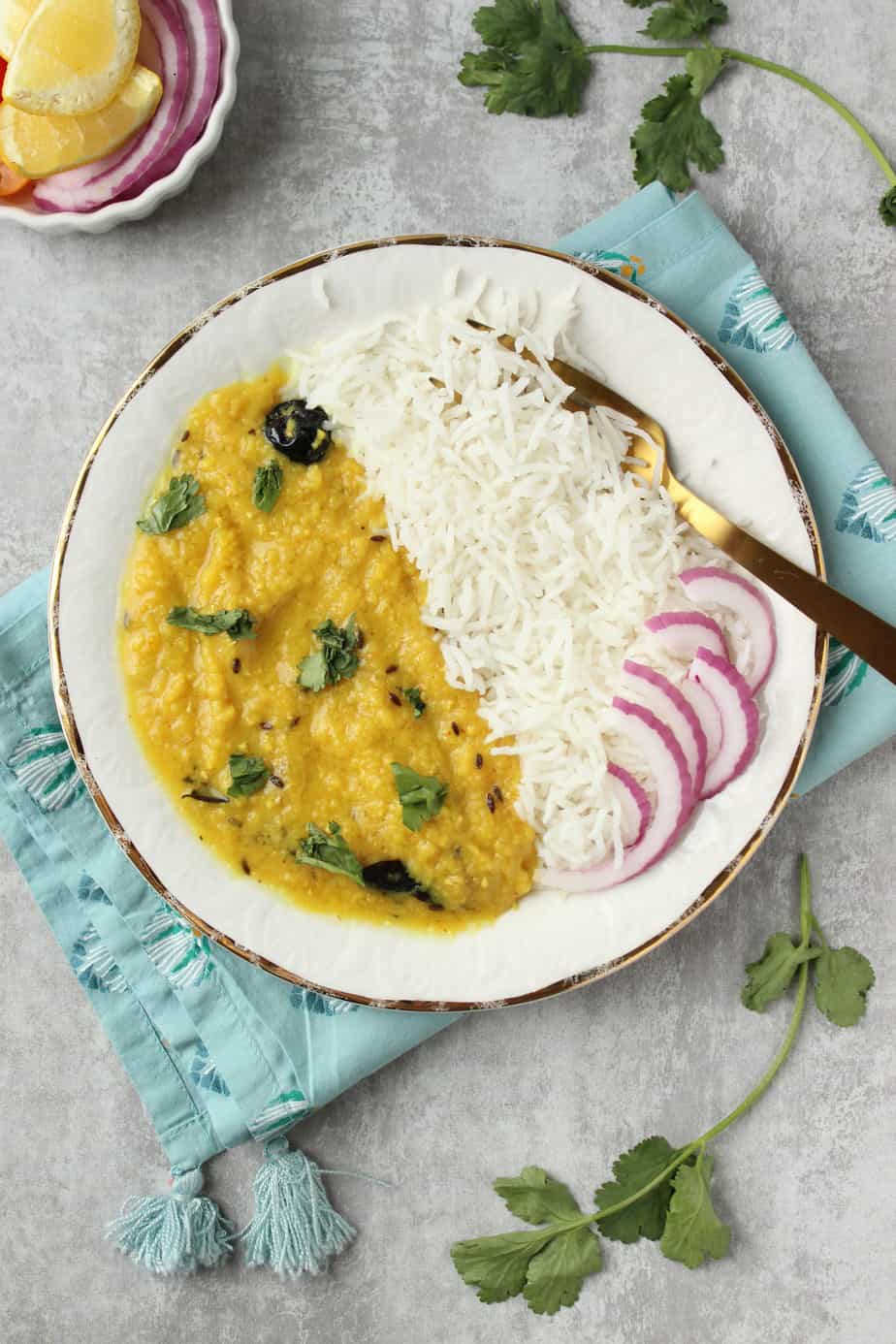 a plate of Khatti Daal with white rice and sliced red onions