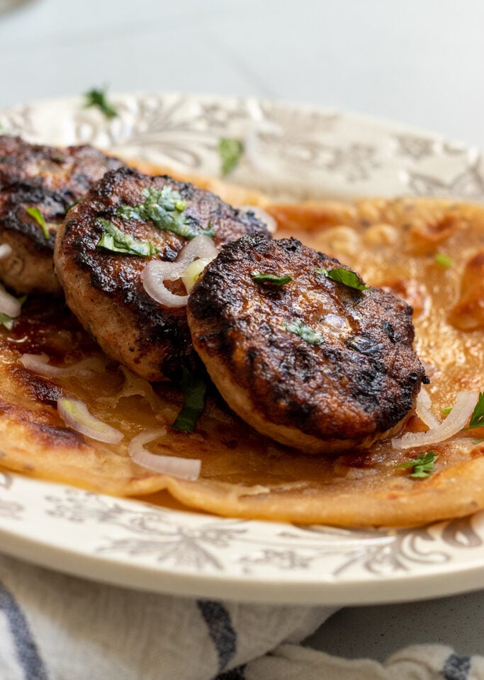 ¾ side view of three chicken kababs on top of a paratha