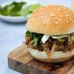 most of a pulled beef slider with lettuce, sauce and some extra greens in the background