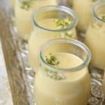 Small glass jars filled with creamy yellow Bread Kheer custard, topped with chopped pistachios, arranged neatly on an ornate silver tray.