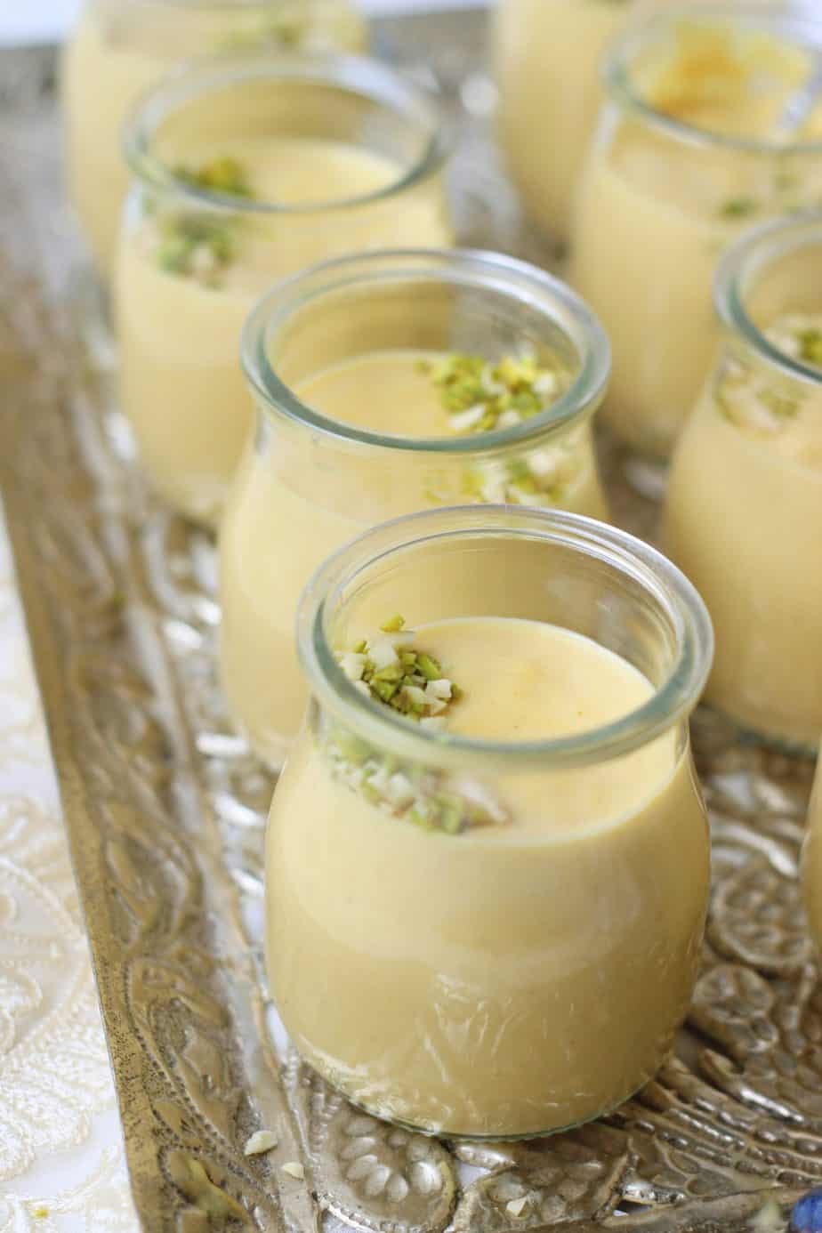 Small glass jars filled with creamy yellow Bread Kheer custard, topped with chopped pistachios, arranged neatly on an ornate silver tray.