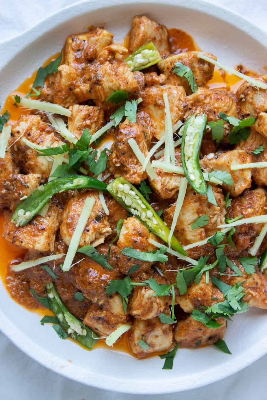 a close up of a dish of Karhai Chicken with green chilies,ciilantro and ginge