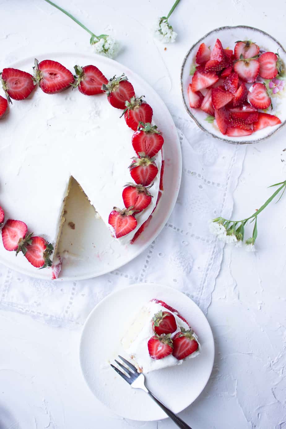 whole round tres leches cake with a slice on a separate plate and a plate of strawberries