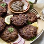 Kachay Qeemay Kay Kabab on a silver platter with parchment paper, chutney and garnishes