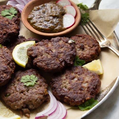 Kachay Qeemay Kay Kabab on a silver platter with parchment paper, chutney and garnishes