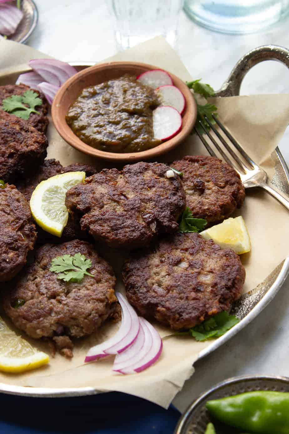 Kachay Qeemay Kay Kabab on a silver platter with parchment paper, chutney and garnishes