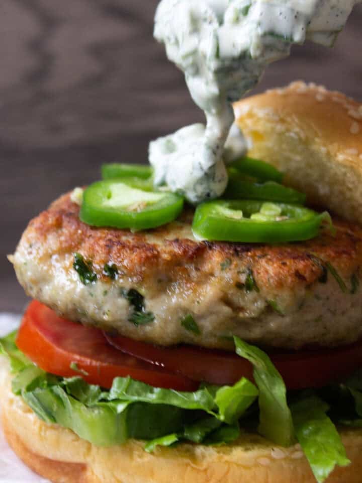 A herbed chicken burger showing three quarters, sauce being poured over top