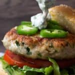 A herbed chicken burger showing three quarters, sauce being poured over top