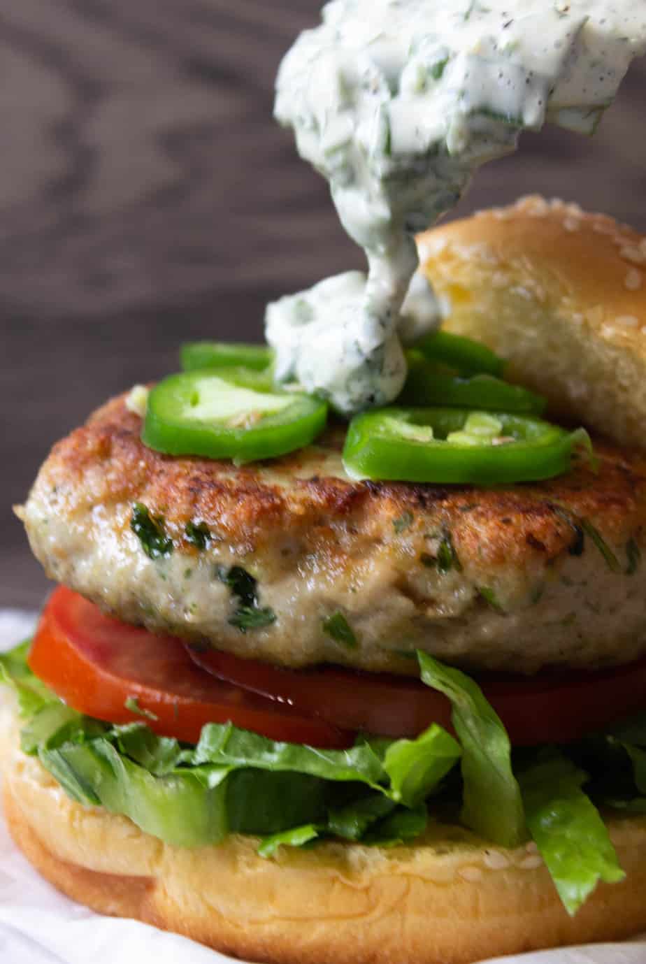 A herbed chicken burger showing three quarters, sauce being poured over top