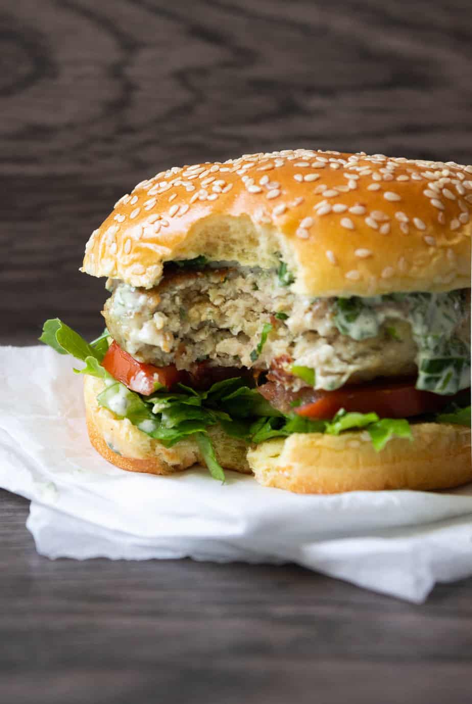 burger with one bite taken out of it sitting on layers of parchment paper