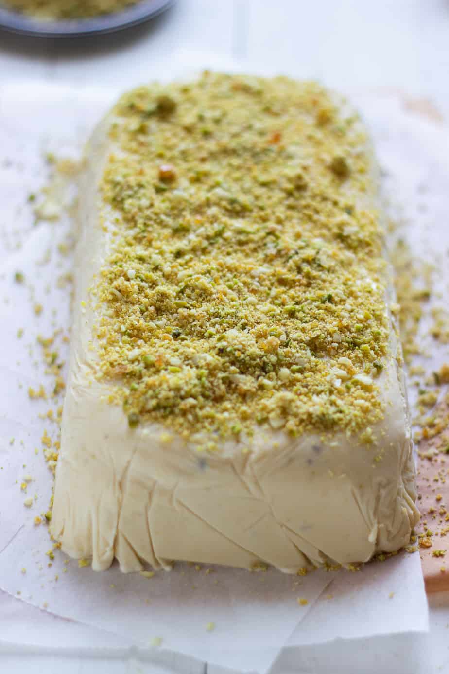 Kulfi frozen in a rectangular container and topped with almond, pistachio and caramel crunch.