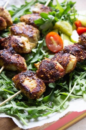 Partial shot of three sesame ginger chicken skewers on a bed of arugula