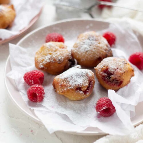 a plate with four raspberry fritters and scattered raspberries