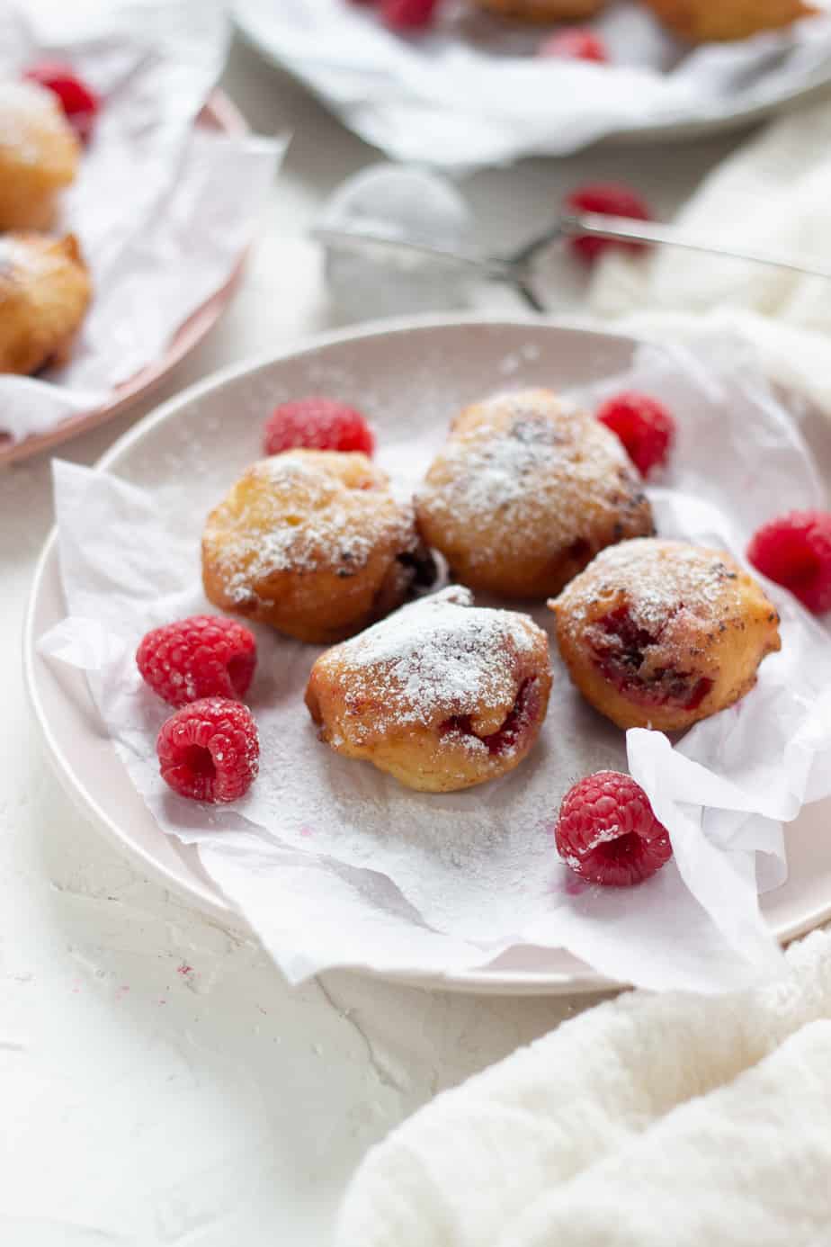 a plate with four raspberry fritters and scattered raspberries