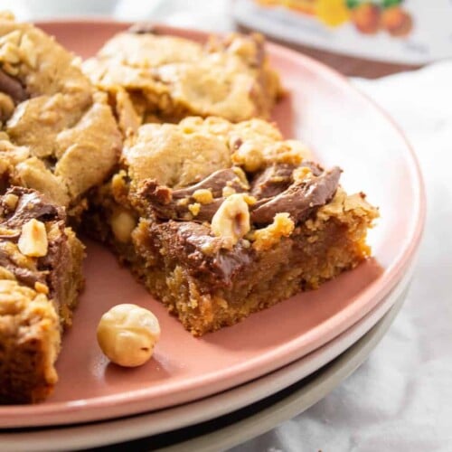 Nutella Blondies on a stack of 3 plates with a partial bottle of Nutella in the background