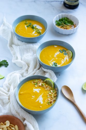 Three bowls of instant pot carrot ginge soup and assorted garnishes
