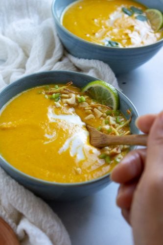 a hand placing a spoon in a bowl of soup as if to take a bite. pictured: instant pot carrot soup in a blue bowl