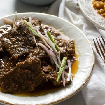 a plate with pasanday garnished with onions and chilies, two bowls of food in the background