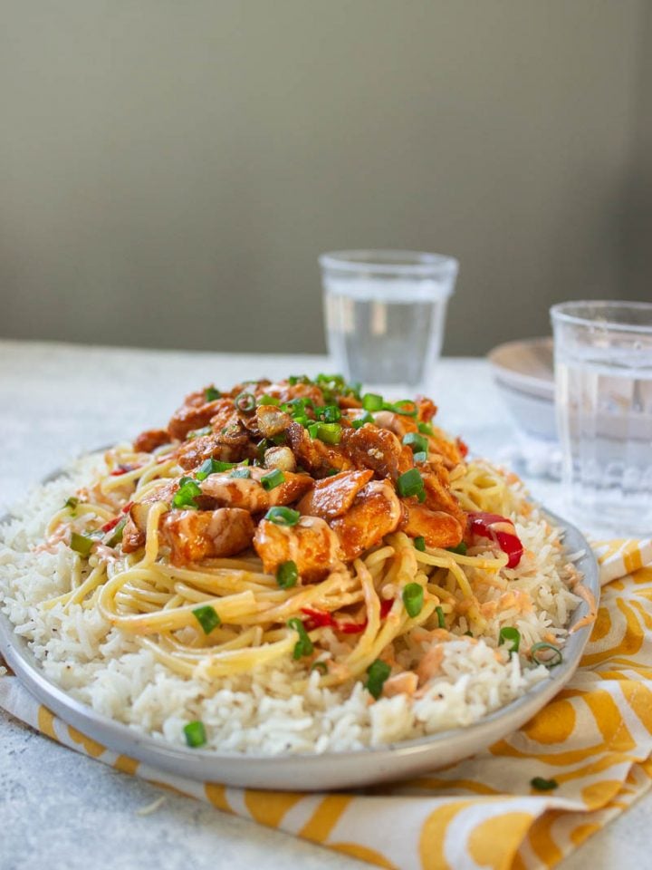 a dish of singaporean rice with two glasses of water in the background