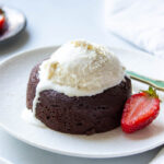 A plate with a lava cake, half a strawberry and melting vanilla ice cream