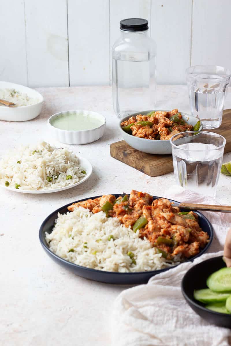 A table set with glasses of water, dishes with chicken jalfrezi and rice in different combinations.
