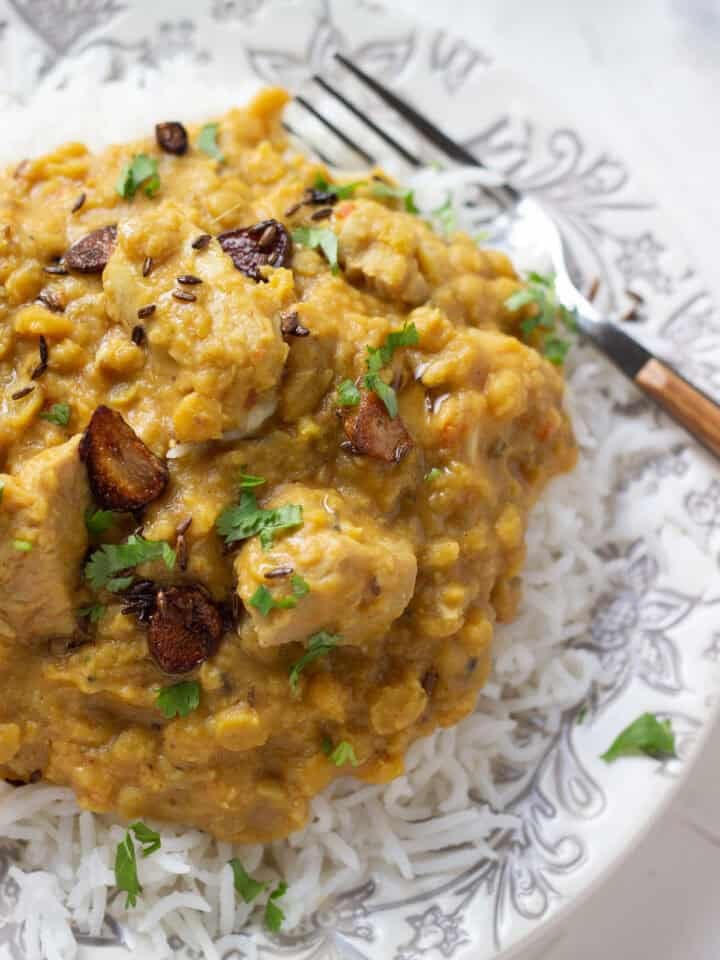 A plate of rice topped with creamy yellow dal chicken, garnished with fried garlic and cilantro. A fork rests on the plate