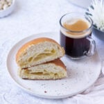 Papaproti Bun halved and on a plate with a cup of coffee. Melted butter centre.