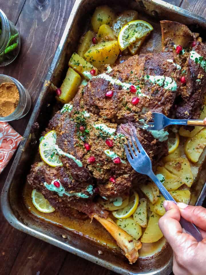 mutton raan roast in a roasting tray with potatoes and garnished with lemon and cilantro