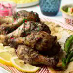 Sumac Chicken Drumsticks on a red dish with pita wedges and slices of lemon