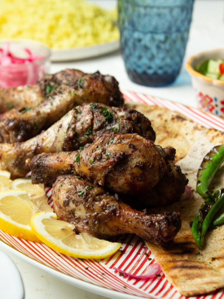 Sumac Chicken Drumsticks on a red dish with pita wedges and slices of lemon
