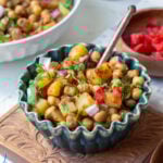 a green bowl of chana chaat on a carved chopping board with a spoon in it
