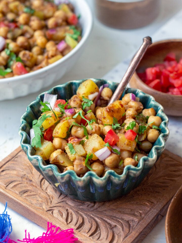 a green bowl of chana chaat on a carved chopping board with a spoon in it