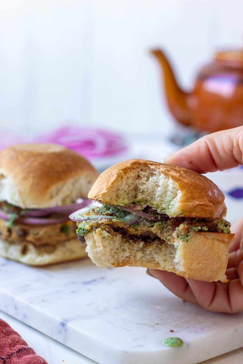 A handheld Bun Kabab with a bite taken out of it, blurred bun kabab in the background