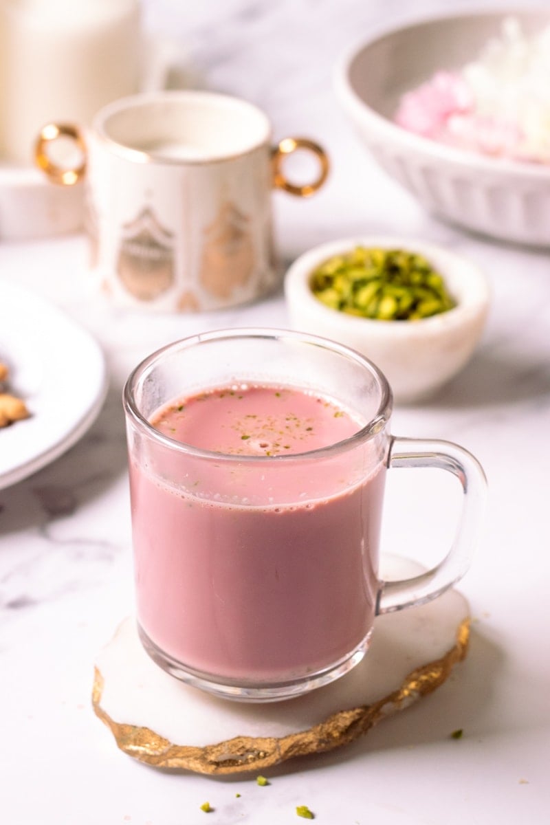 a cup of kashmiri chai on a marble coaster with nuts and sugar and flowers in the background