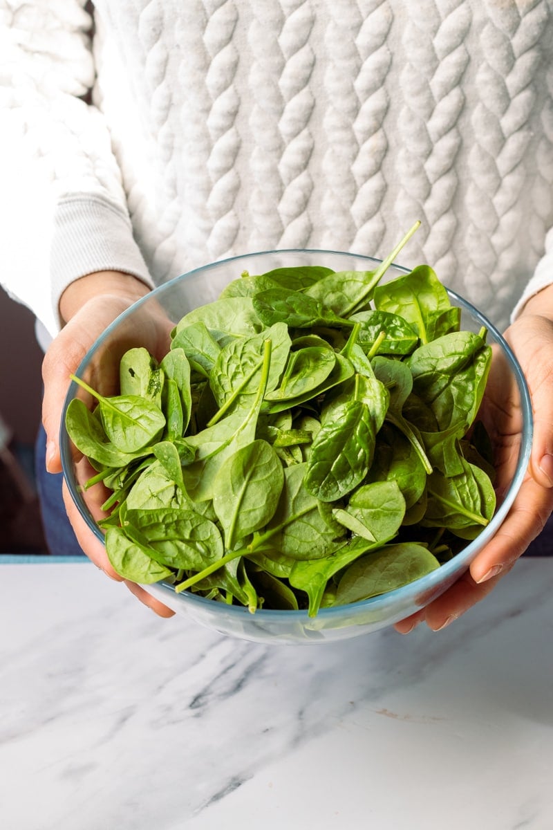 A bowl of baby spinach being held up