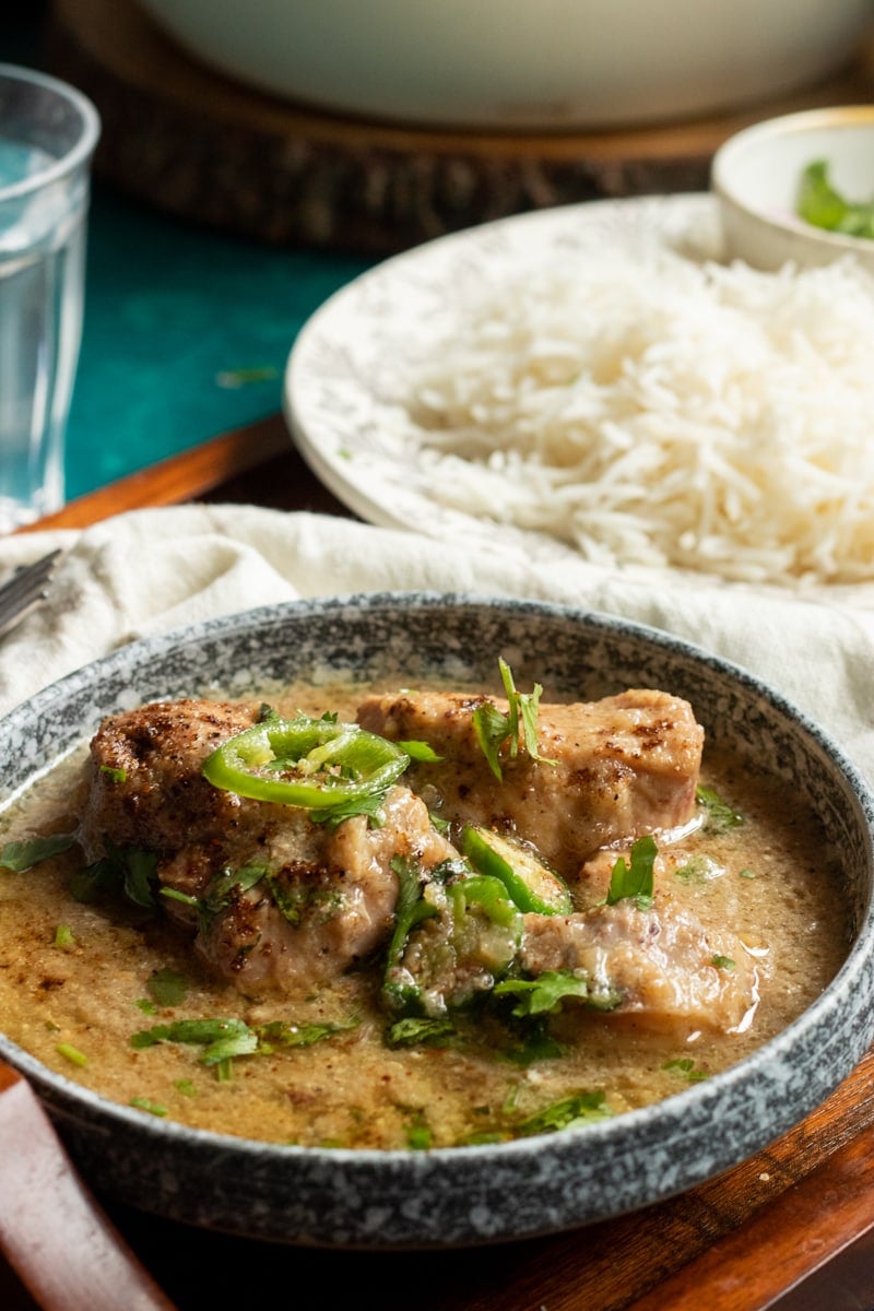 white chicken curry or salan in a bowl, a plate of rice in the background