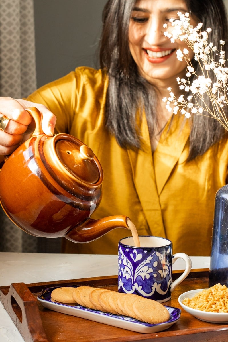 Sarah Mir, Pakistani Food Blogger, pouring chai from a brown teapot into a blue mug.